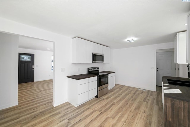 kitchen featuring white cabinetry, baseboards, appliances with stainless steel finishes, light wood finished floors, and dark countertops