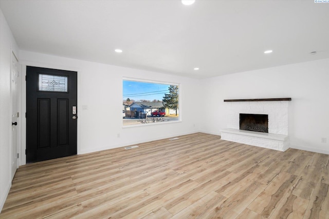 unfurnished living room with light wood finished floors, a brick fireplace, and recessed lighting