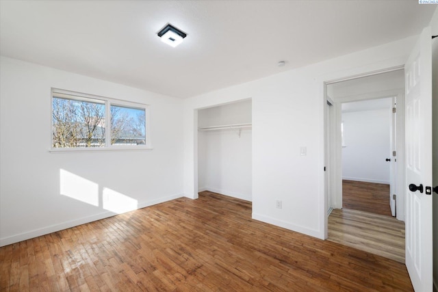 unfurnished bedroom with a closet, hardwood / wood-style flooring, and baseboards