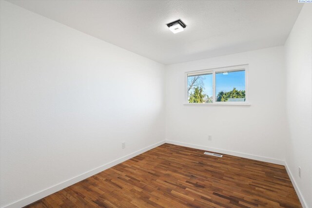 empty room featuring wood finished floors, visible vents, and baseboards