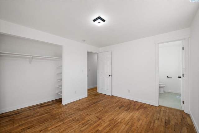 unfurnished bedroom with a closet, baseboards, hardwood / wood-style floors, and ensuite bathroom