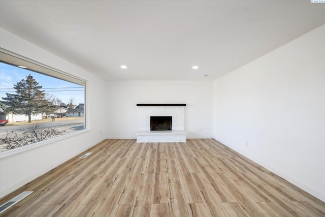 unfurnished living room with a fireplace with raised hearth, recessed lighting, visible vents, baseboards, and light wood finished floors