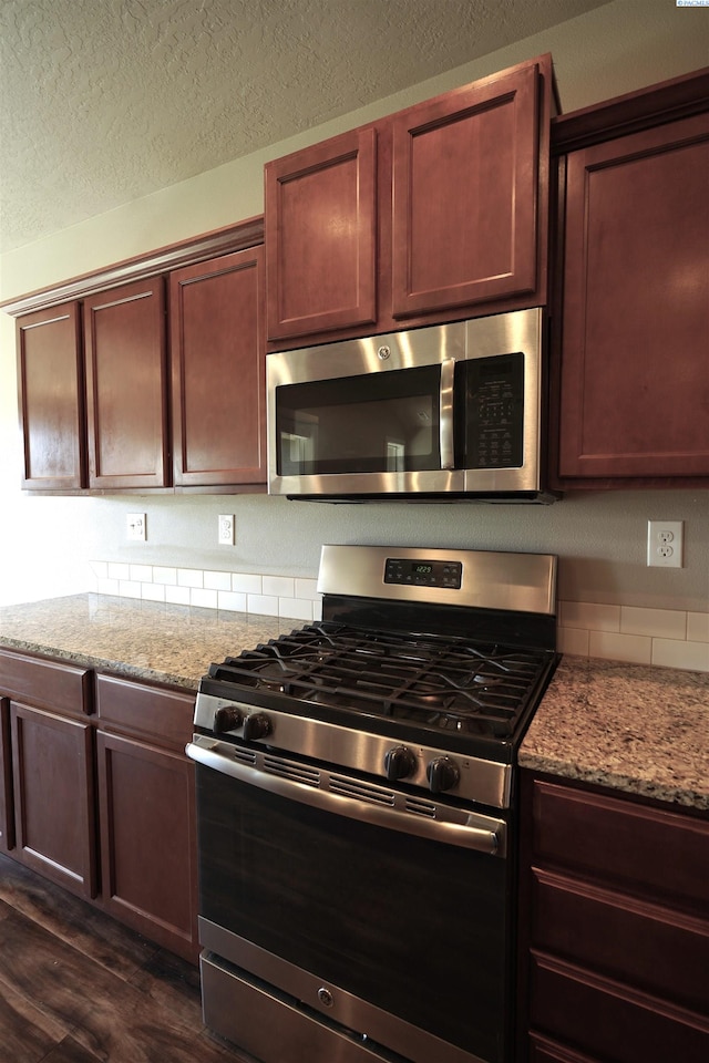 kitchen with light stone countertops, stainless steel appliances, backsplash, and dark wood-style flooring