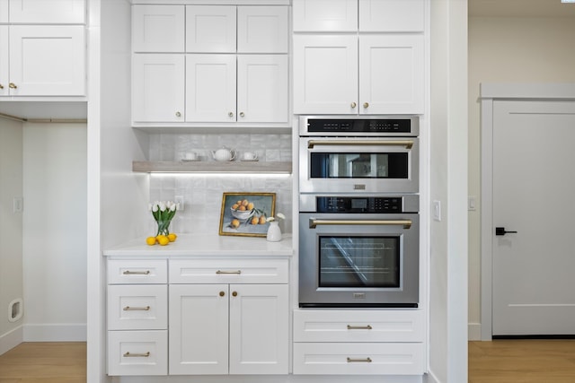 kitchen featuring tasteful backsplash, light wood-style flooring, light countertops, stainless steel double oven, and white cabinetry