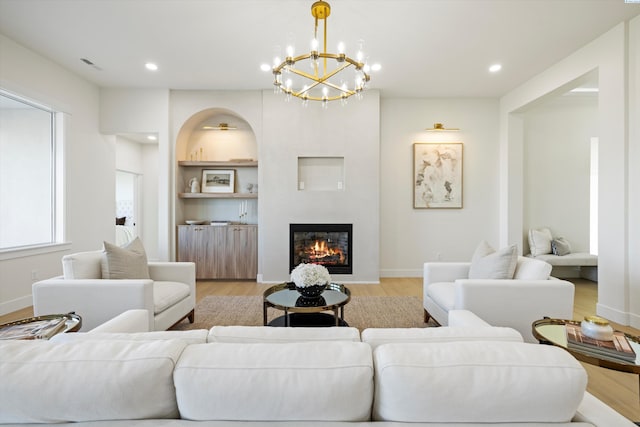 living room featuring built in features, light wood finished floors, recessed lighting, visible vents, and a glass covered fireplace