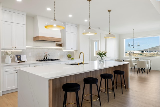 kitchen with decorative backsplash, an island with sink, custom range hood, gas cooktop, and a sink