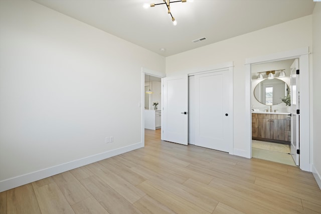 unfurnished bedroom featuring baseboards, visible vents, light wood-style flooring, ensuite bathroom, and a closet