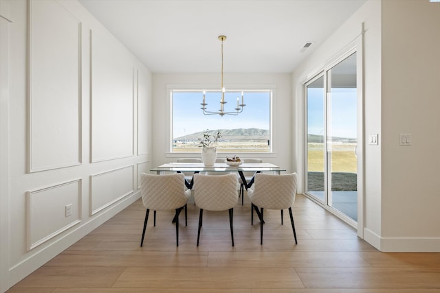 dining room featuring a chandelier, light wood-type flooring, baseboards, and a decorative wall