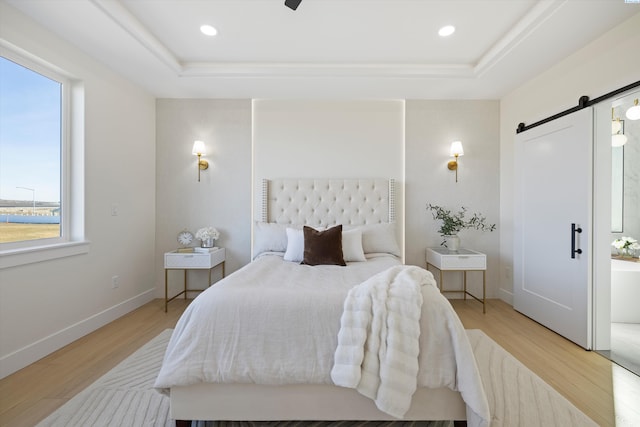 bedroom with light wood finished floors, a tray ceiling, a barn door, and baseboards