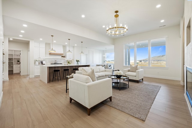 living room with recessed lighting, an inviting chandelier, light wood-style floors, a glass covered fireplace, and baseboards