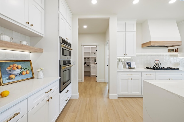 kitchen with black cooktop, custom range hood, white cabinetry, and tasteful backsplash