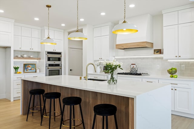 kitchen with double oven, premium range hood, a sink, white cabinets, and tasteful backsplash