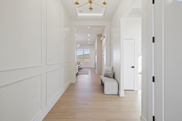 corridor featuring a notable chandelier, recessed lighting, a raised ceiling, a decorative wall, and light wood-style flooring