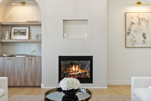 living area featuring wood finished floors, a glass covered fireplace, and baseboards