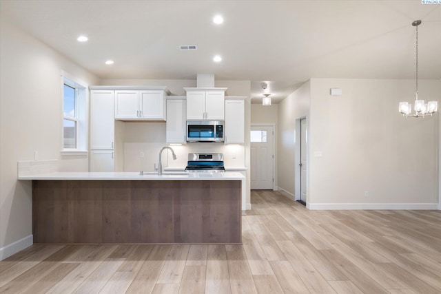 kitchen featuring white cabinetry, sink, hanging light fixtures, light hardwood / wood-style floors, and stainless steel appliances