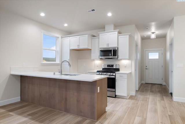 kitchen featuring sink, appliances with stainless steel finishes, white cabinetry, backsplash, and light hardwood / wood-style floors