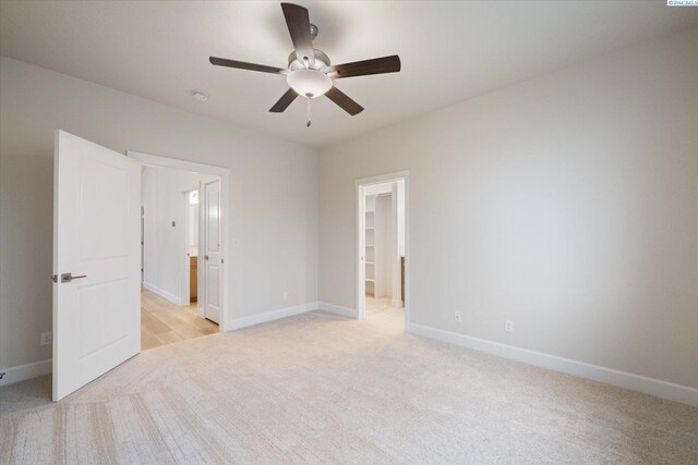 unfurnished bedroom with ensuite bathroom, a spacious closet, ceiling fan, light carpet, and a closet