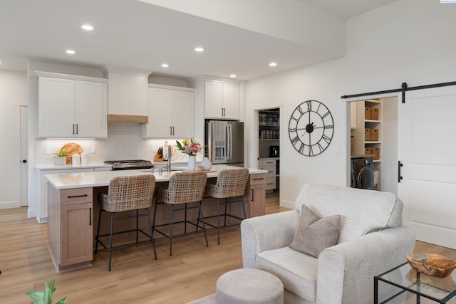 kitchen featuring washer / clothes dryer, light wood-style floors, stainless steel appliances, light countertops, and a kitchen bar