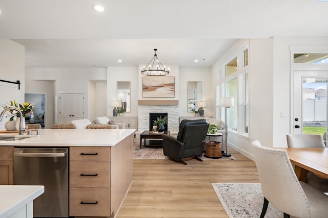 kitchen featuring stainless steel dishwasher, a sink, light countertops, open floor plan, and light wood-type flooring