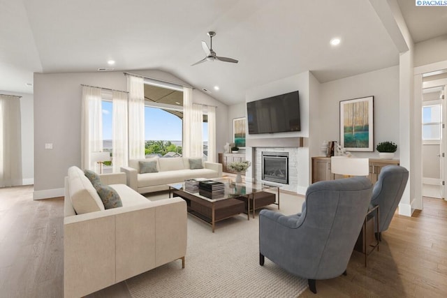 living area with lofted ceiling, light wood-type flooring, a glass covered fireplace, and recessed lighting