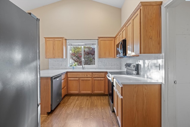 kitchen featuring lofted ceiling, sink, appliances with stainless steel finishes, light hardwood / wood-style floors, and backsplash