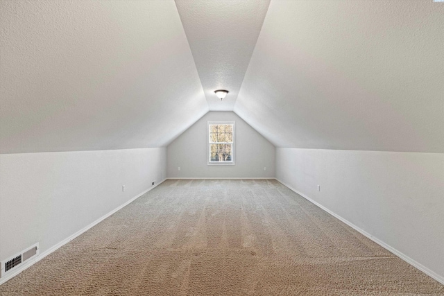 additional living space with vaulted ceiling, carpet flooring, and a textured ceiling