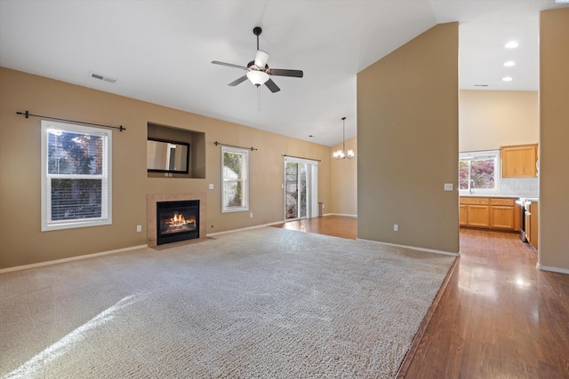 unfurnished living room with a tiled fireplace, ceiling fan with notable chandelier, plenty of natural light, and light hardwood / wood-style flooring