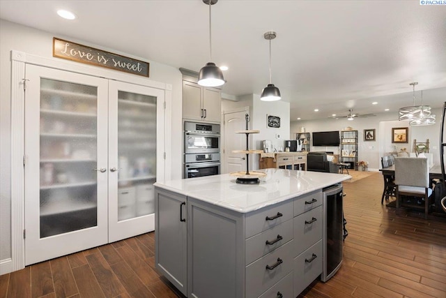 kitchen with gray cabinetry, double oven, dark wood-type flooring, a kitchen island, and light countertops