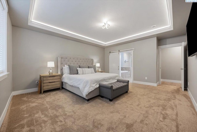 carpeted bedroom featuring a barn door, ensuite bathroom, and a tray ceiling