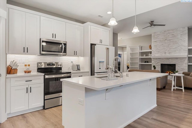 kitchen with stainless steel appliances, white cabinetry, a center island with sink, and pendant lighting