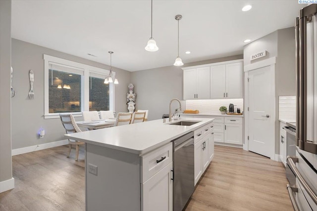 kitchen with pendant lighting, white cabinetry, a kitchen island with sink, stainless steel dishwasher, and light hardwood / wood-style flooring