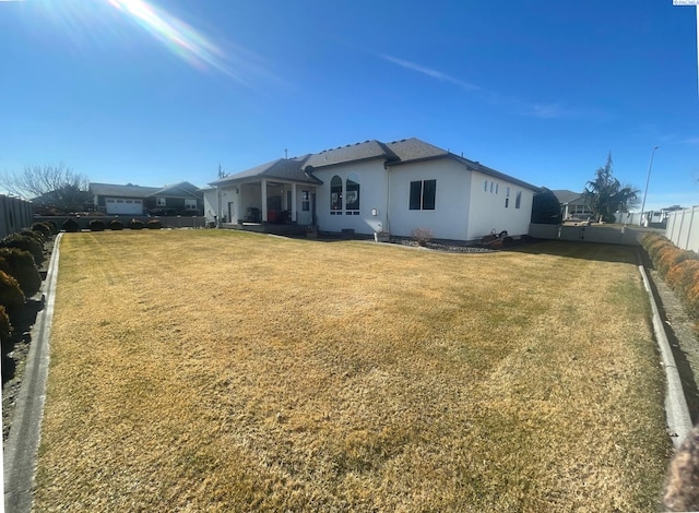 rear view of property with a fenced backyard, a yard, and stucco siding