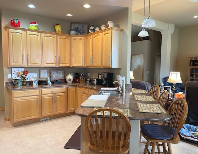 kitchen with a breakfast bar area, a peninsula, a sink, dark stone counters, and decorative light fixtures