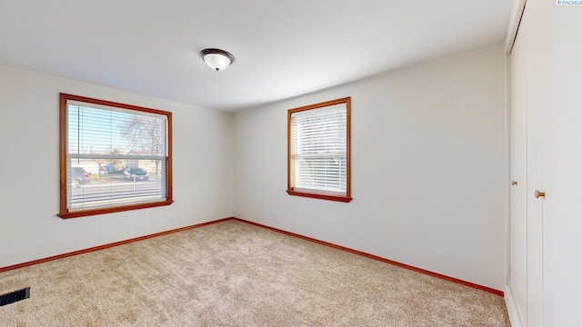 empty room featuring light carpet, visible vents, and baseboards