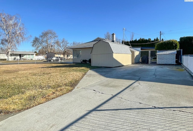 view of side of property with a storage unit, a lawn, a gambrel roof, fence, and an outdoor structure