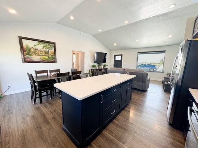 kitchen with stainless steel fridge, a center island, a textured ceiling, dark hardwood / wood-style flooring, and vaulted ceiling