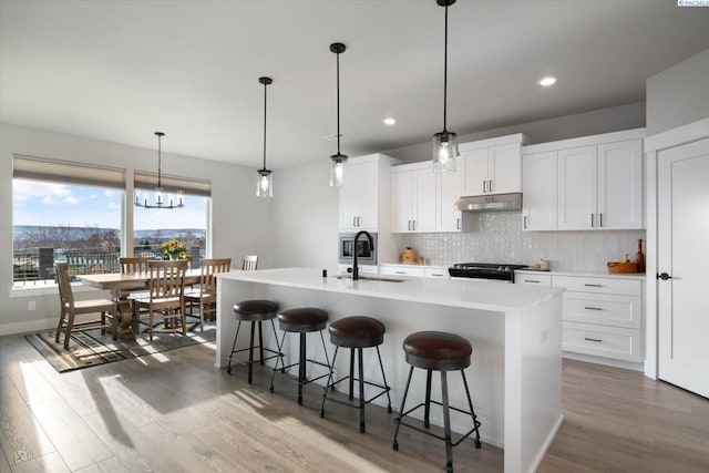 kitchen with white cabinetry, a kitchen breakfast bar, hanging light fixtures, a kitchen island with sink, and range