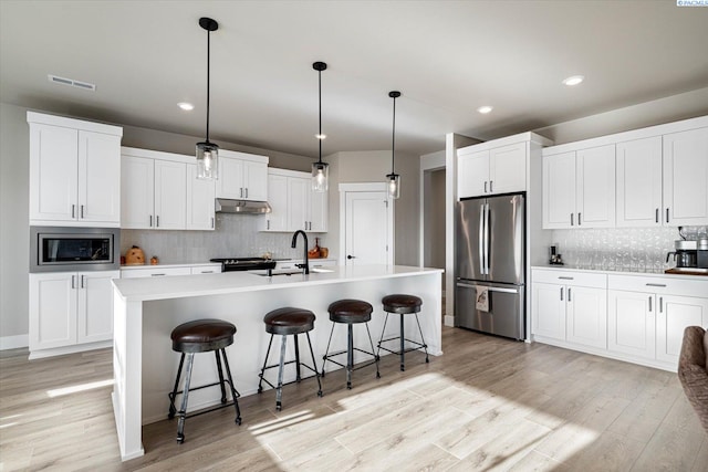 kitchen with stainless steel appliances, an island with sink, and white cabinets