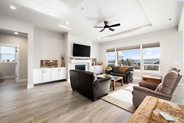 living room featuring a raised ceiling, ceiling fan, and light hardwood / wood-style flooring