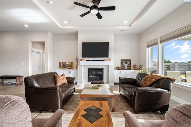 living room featuring hardwood / wood-style floors, a tile fireplace, a raised ceiling, and ceiling fan