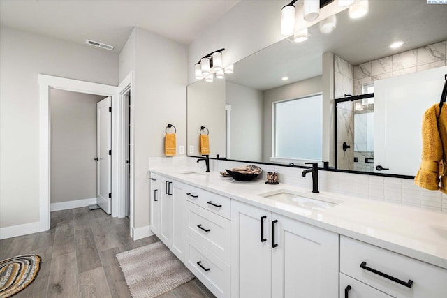 bathroom with hardwood / wood-style flooring, vanity, a shower with shower door, and backsplash