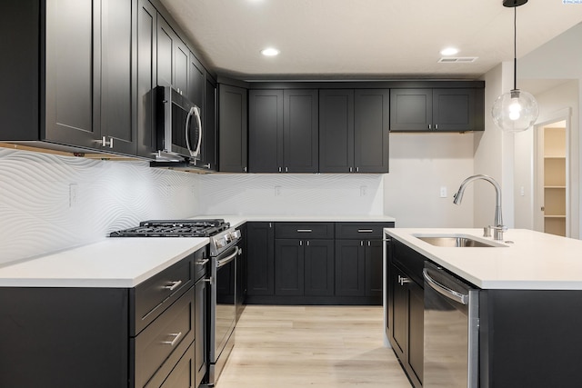 kitchen featuring light wood-type flooring, a center island with sink, sink, appliances with stainless steel finishes, and pendant lighting