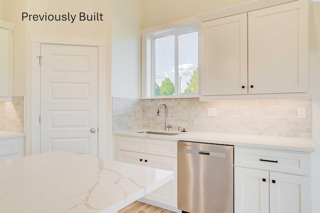 kitchen featuring light stone countertops, decorative backsplash, stainless steel dishwasher, white cabinetry, and a sink