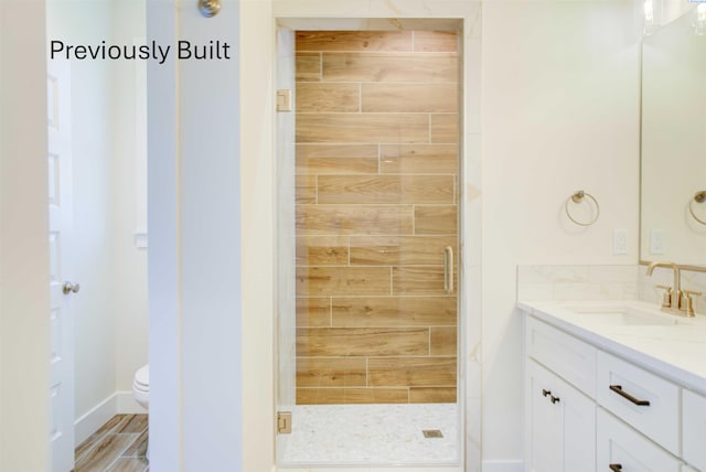 bathroom with wood finished floors, toilet, a stall shower, and vanity