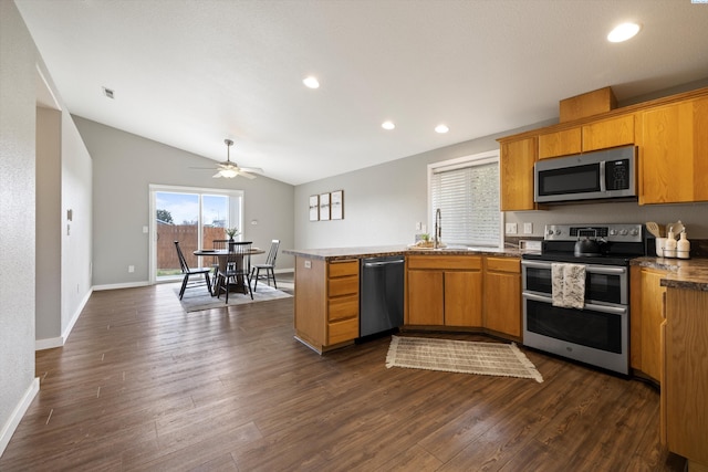 kitchen featuring dark wood-style flooring, brown cabinets, appliances with stainless steel finishes, a sink, and a peninsula