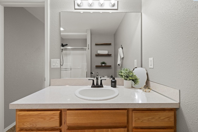 full bath with a textured wall, a stall shower, and vanity