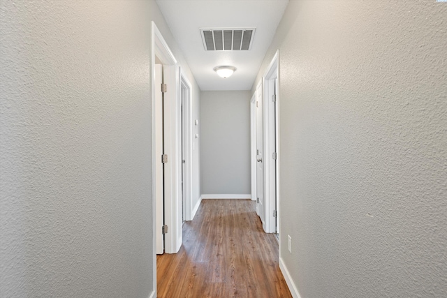 hallway featuring a textured wall, wood finished floors, visible vents, and baseboards