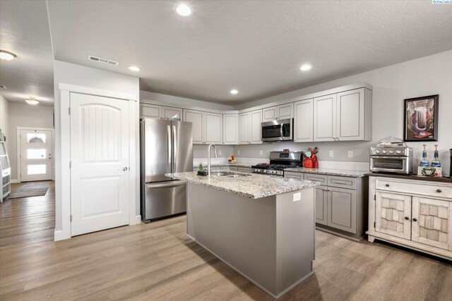kitchen featuring visible vents, light stone countertops, a sink, light wood-style flooring, and appliances with stainless steel finishes