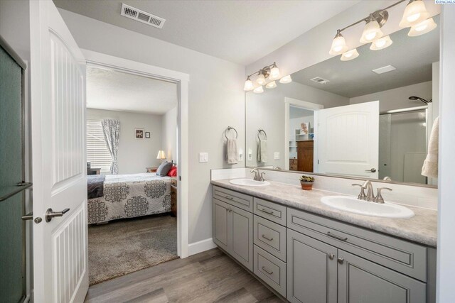 ensuite bathroom featuring a sink, ensuite bath, wood finished floors, and visible vents