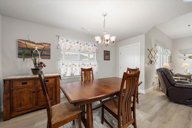 dining space with baseboards, an inviting chandelier, visible vents, and light wood-style floors